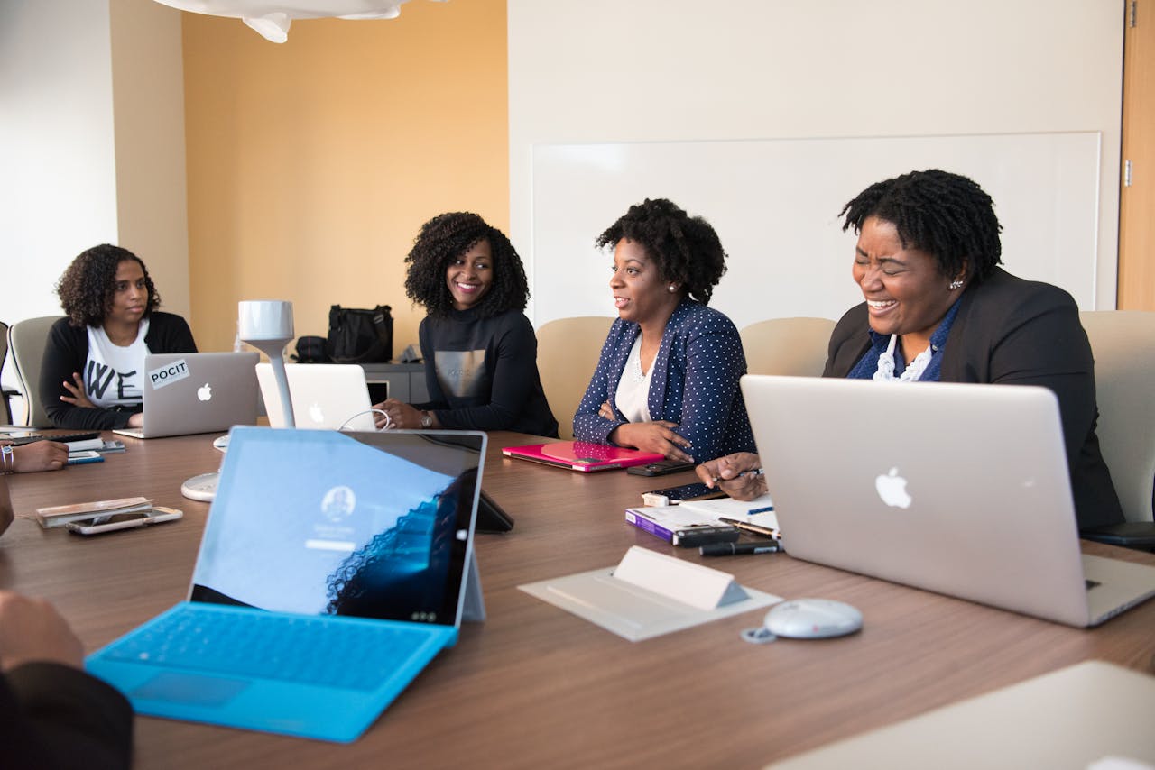 Group of women engaged in a collaborative meeting at an office table with laptops.